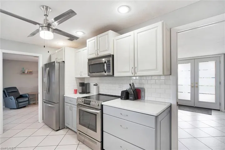 Kitchen with  stainless steel appliances, light tile patterned floors, decorative subway tile backsplash, and white cabinets and grey with raised panel doors.