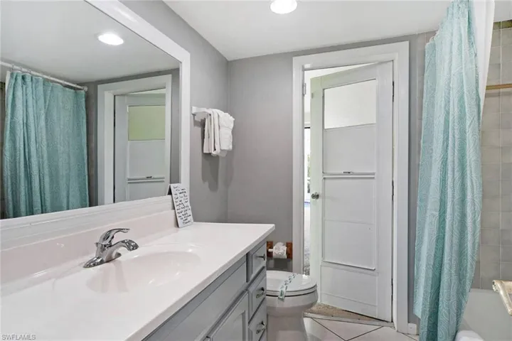 Full bathroom with tile patterned floors, vanity, toilet, and shower / tub combo with curtain access to pool and patio area.