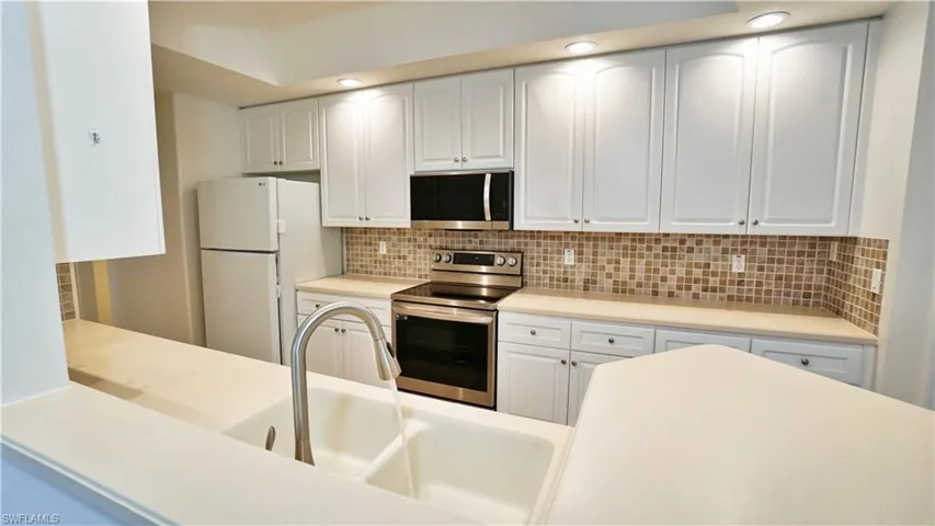Kitchen with light countertops, a sink, tasteful backsplash, stainless steel appliances, and white cabinets