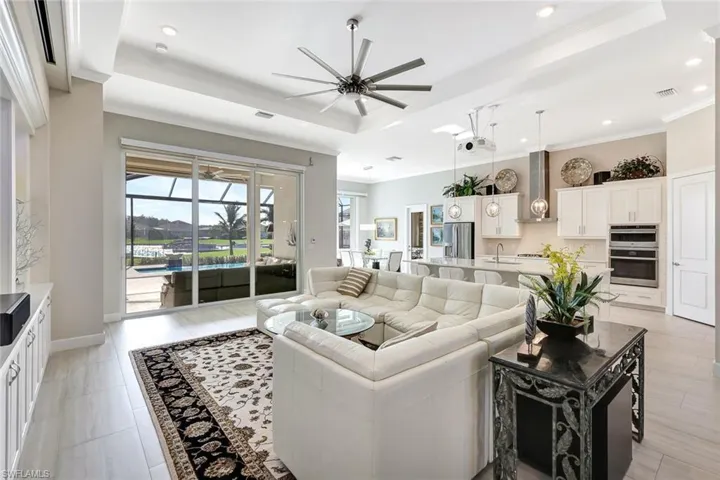 Living room featuring ceiling fan, sink, a tray ceiling, light tile patterned floors, and ornamental molding