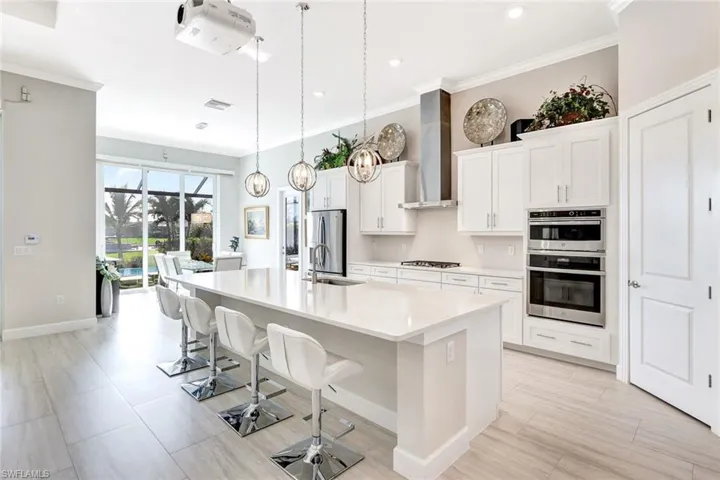 Kitchen featuring wall chimney exhaust hood, stainless steel appliances, a large island with sink, pendant lighting, and white cabinets