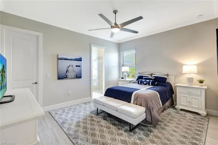Bedroom with ceiling fan, light hardwood / wood-style flooring, crown molding, and ensuite bath