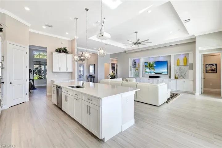 Kitchen with pendant lighting, a center island with sink, ceiling fan with notable chandelier, sink, and white cabinetry
