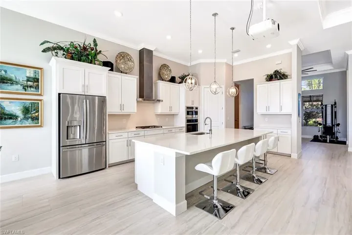 Kitchen featuring white cabinetry, an island with sink, wall chimney range hood, and appliances with stainless steel finishes