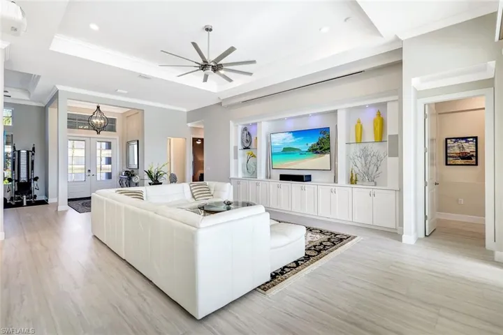 Living room with french doors, ceiling fan with notable chandelier, a raised ceiling, light hardwood / wood-style flooring, and ornamental molding