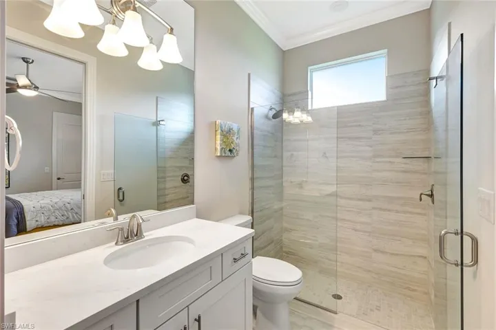 Bathroom with vanity, ceiling fan with notable chandelier, crown molding, toilet, and an enclosed shower