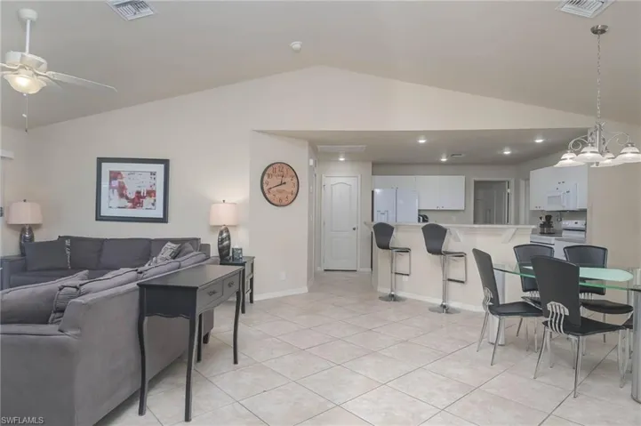 Living room featuring vaulted ceiling, ceiling fan with notable chandelier, and light tile patterned floors