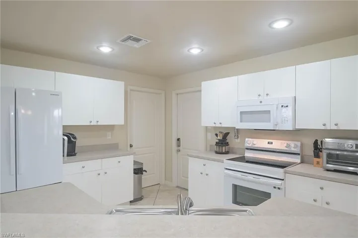 Kitchen with sink, white cabinets, white appliances, and light tile patterned flooring