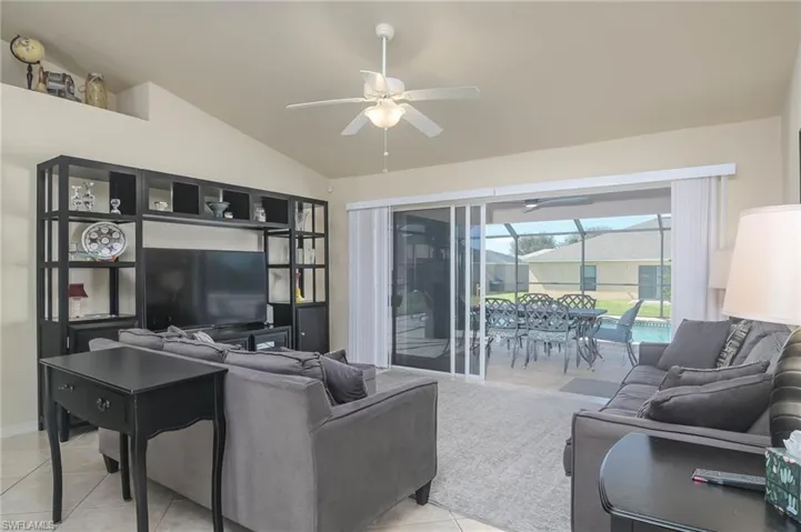 Living room featuring vaulted ceiling, ceiling fan, and light tile patterned floors