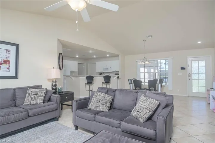 Tiled living room featuring high vaulted ceiling and ceiling fan with notable chandelier