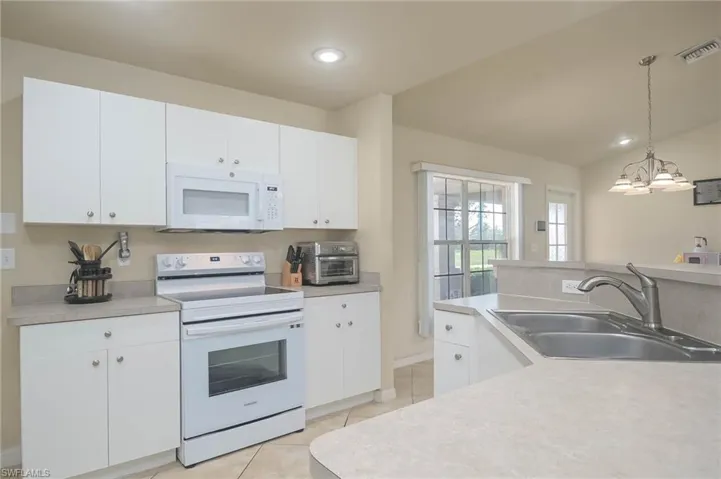 Kitchen featuring white cabinets, a chandelier, pendant lighting, sink, and white appliances