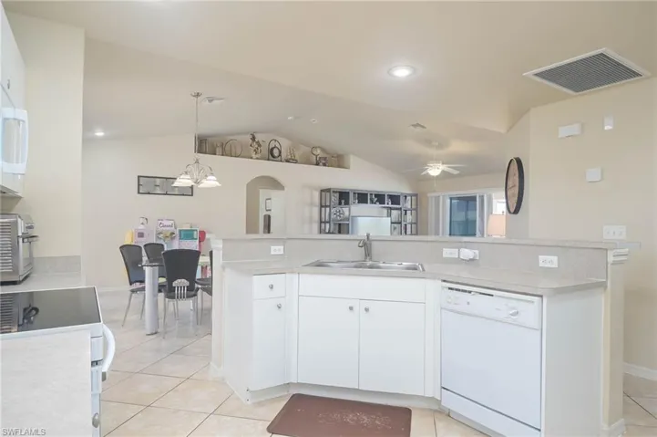 Kitchen with white cabinetry, white dishwasher, lofted ceiling, and decorative light fixtures