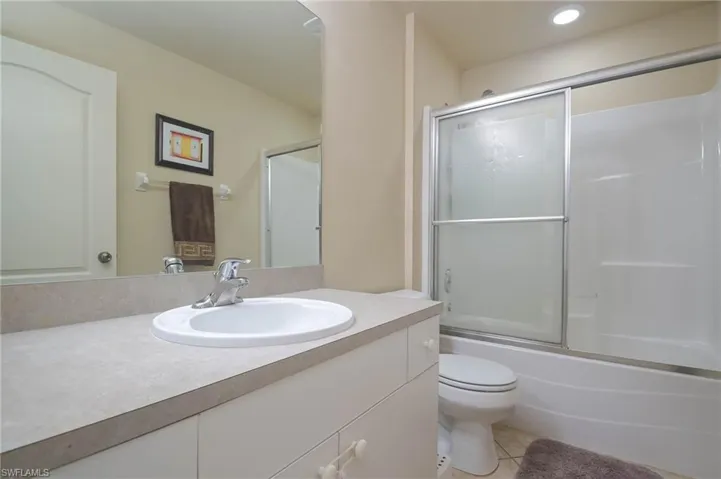 Full bathroom with vanity, bath / shower combo with glass door, toilet, and tile patterned floors
