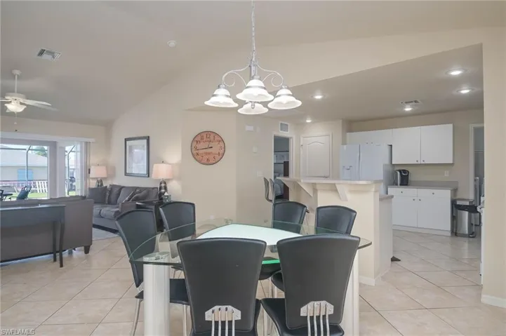 Dining space featuring vaulted ceiling, ceiling fan with notable chandelier, and light tile patterned floors