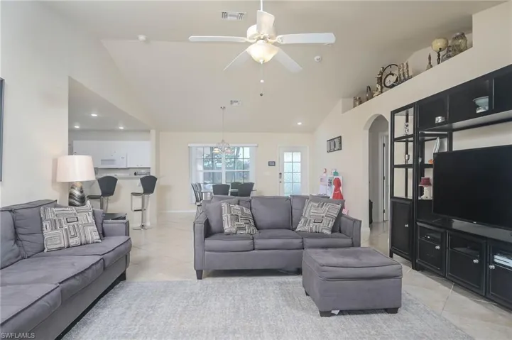 Tiled living room with high vaulted ceiling and ceiling fan with notable chandelier