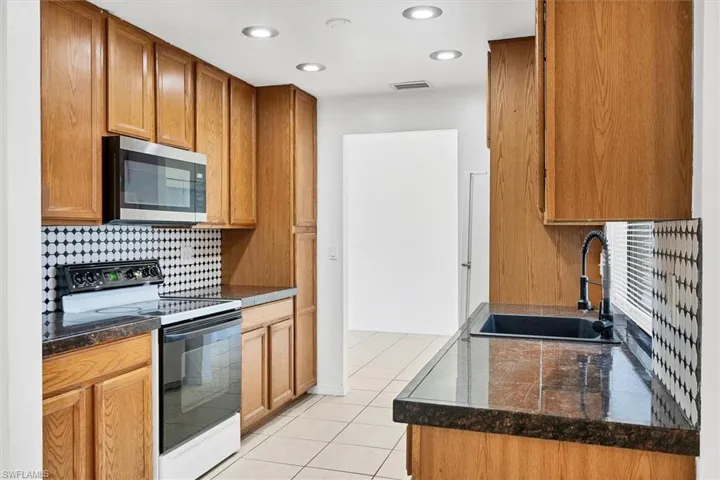 Kitchen with sink, backsplash, white electric range, and light tile patterned floors