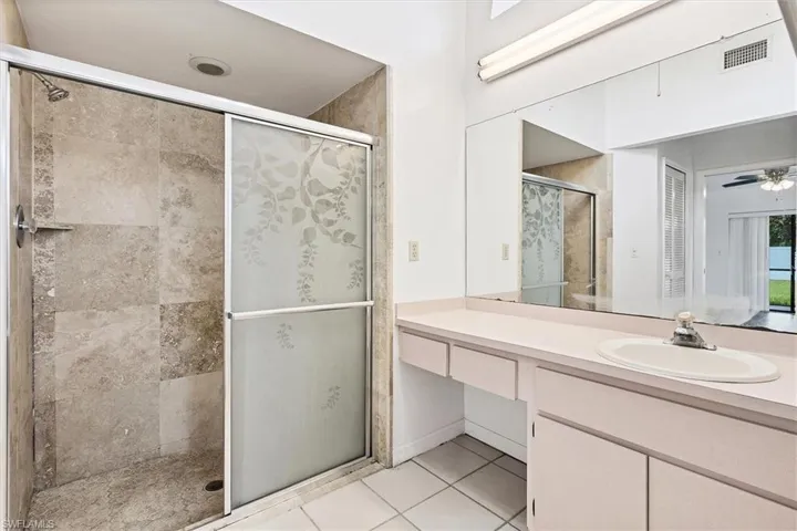 Bathroom featuring ceiling fan, vanity, tile patterned flooring, and an enclosed shower