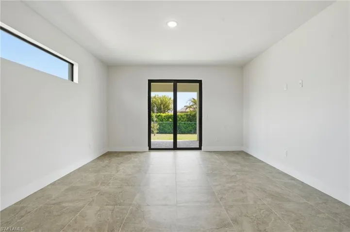 Spacious interior featuring a sliding glass door, transom window, recessed ceiling lighting, light-toned tile flooring, and white baseboards
