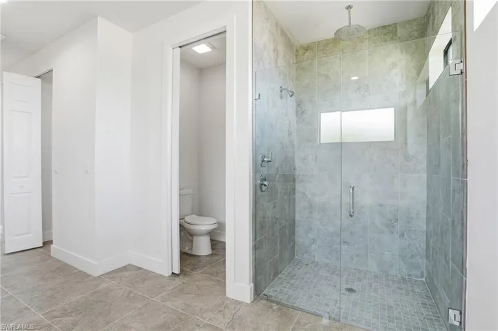 Glass-enclosed shower featuring a rainfall showerhead, wall-mounted fixtures, and a transom window, all surrounded by large format tile