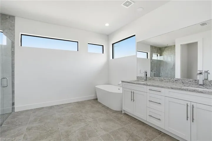 Spacious bathroom featuring a dual vanity with white cabinetry and stone countertops