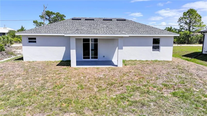 Back of house with roof with shingles, a yard, a patio, and stucco siding