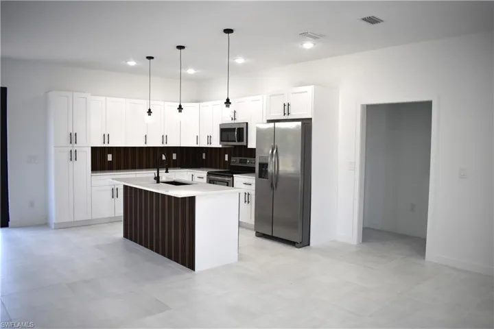 Modern kitchen featuring white shaker cabinetry, stainless steel appliances, a center island with a wood-finish accent panel, and black pendant lighting