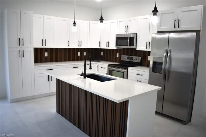 Kitchen featuring white shaker cabinetry, stainless steel appliances, a wood-slat backsplash, a central island with a solid surface countertop, and pendant lighting