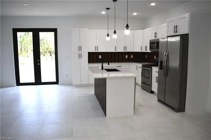 Modern kitchen featuring white shaker cabinetry, stainless steel appliances, a center island with sink, and light tile flooring
