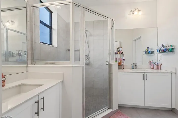 Bathroom with a stall shower, two vanities, and light tile patterned floors
