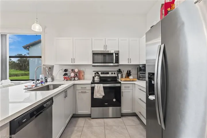 Kitchen featuring stainless steel appliances, hanging light fixtures, light tile patterned floors, white cabinetry, and light stone counters