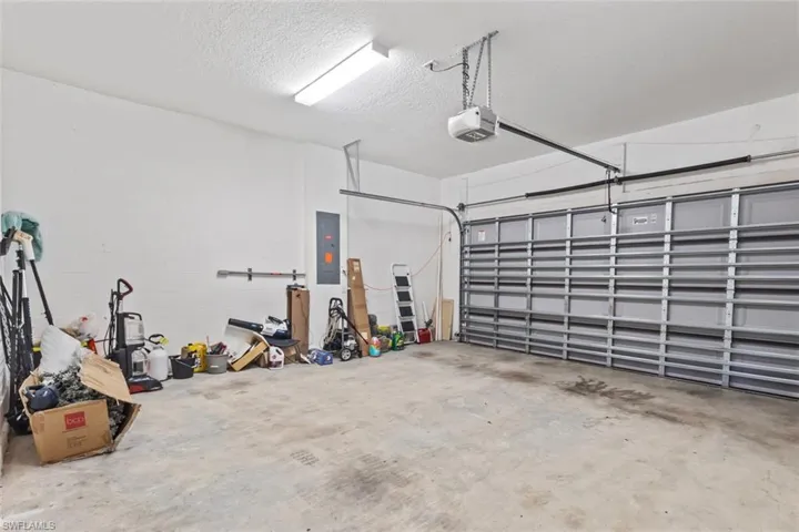 Garage featuring electric panel, a garage door opener, and concrete block wall
