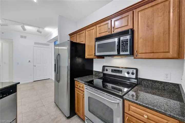 Stainless steel appliances, wood-finish cabinetry, dark granite countertops, built-in microwave, and tile flooring