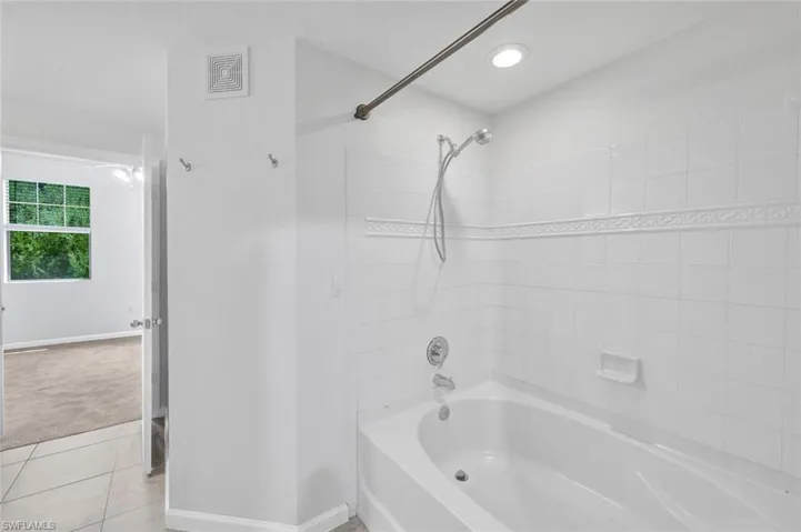 Large tub and shower combination with white tile with decorative accent, and recessed lighting