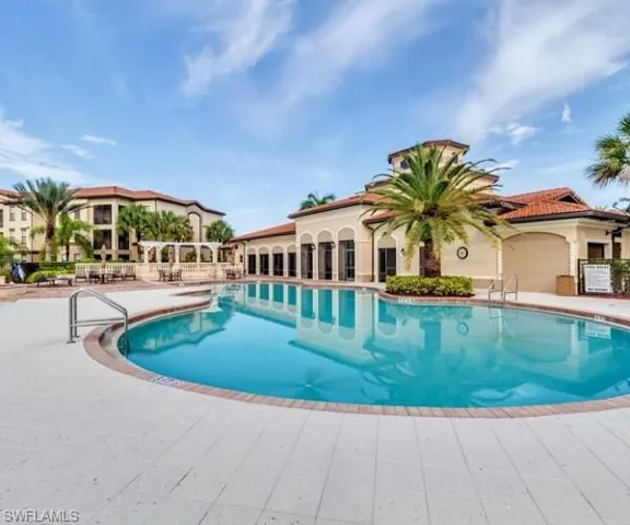 Expansive swimming pool with a surrounding paver deck, a pool house with arched windows, and lush landscaping