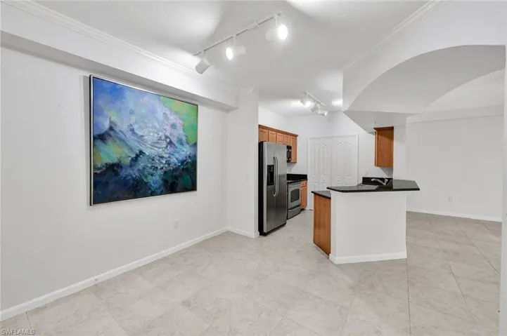 Open-concept dining, kitchen, and living area with tile flooring, crown molding, and track lighting