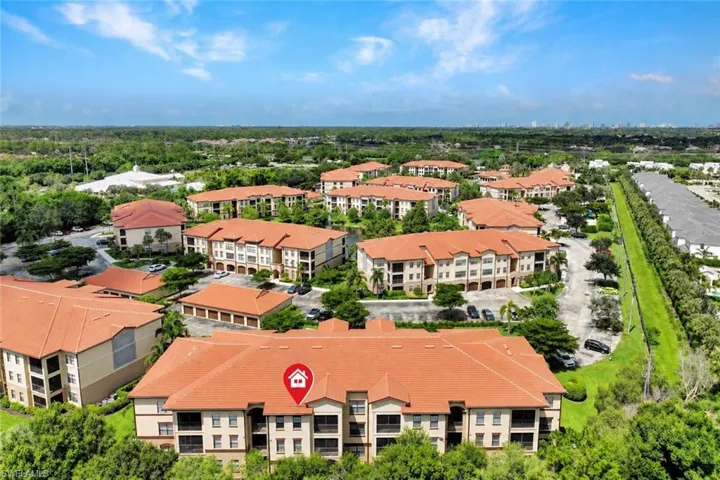 Community setting featuring multiple residential buildings with terracotta-style roofs, surrounded by mature trees and landscaping