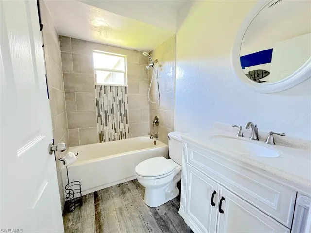 Full bathroom featuring tiled shower / bath, vanity, toilet, and wood-style tile floors