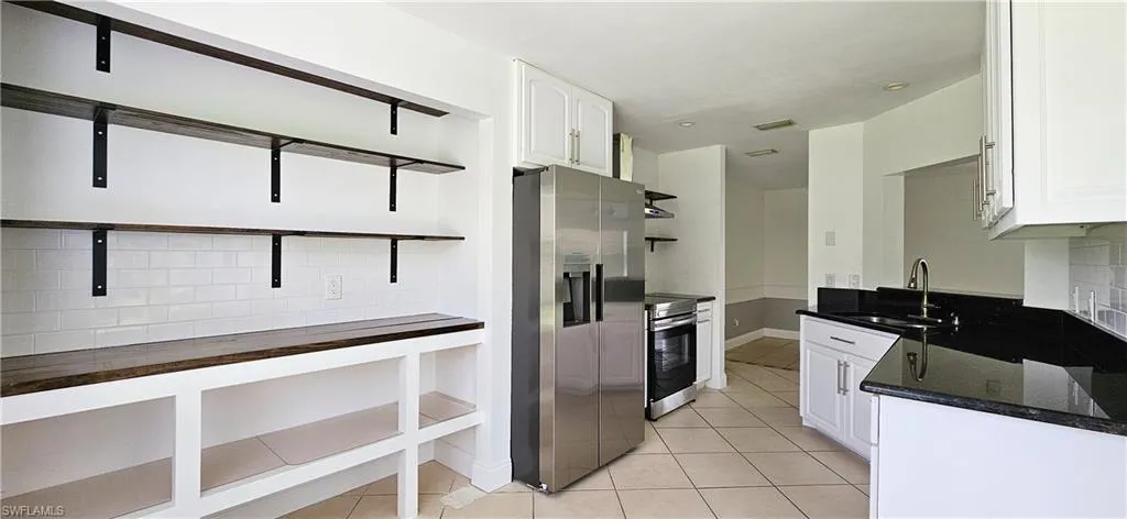 Kitchen with granite countertops, backsplash, appliances with stainless steel finishes, white cabinetry, and sink