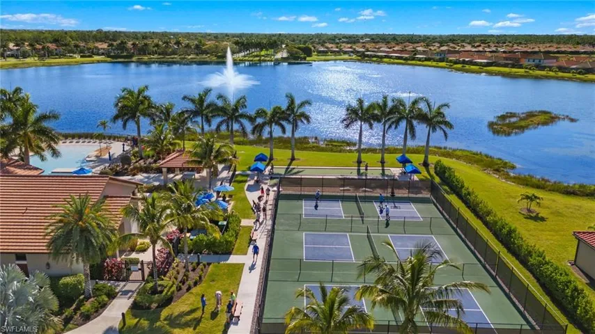 Expansive community amenities featuring multiple pickleball courts, a large lake with fountain, mature palm trees, lush landscaping, and a clubhouse with a terracotta tile roof
