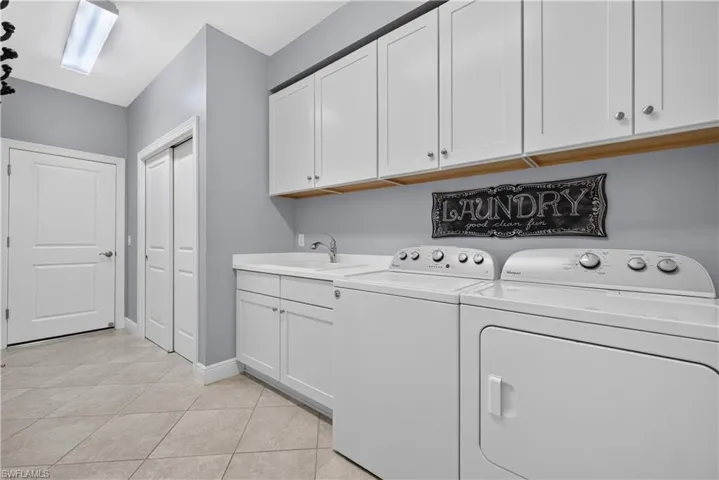 Dedicated laundry room featuring white cabinetry, a utility sink, and light tile flooring