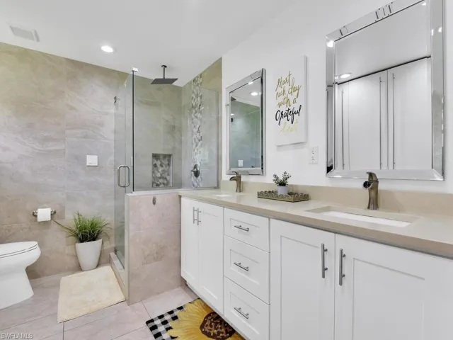 Bathroom with an enclosed shower, tile patterned flooring, tile walls, vanity, and toilet