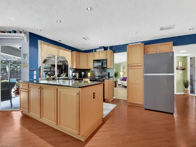 Kitchen with dark stone counters, backsplash, a kitchen island, appliances with stainless steel finishes, and light hardwood / wood-style floors