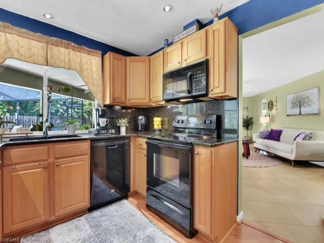 Kitchen with light tile patterned flooring, backsplash, sink, and black appliances