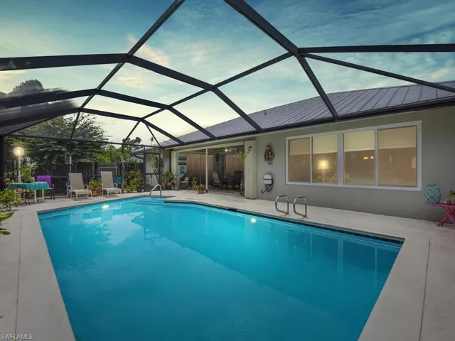 Pool at dusk featuring glass enclosure and a patio