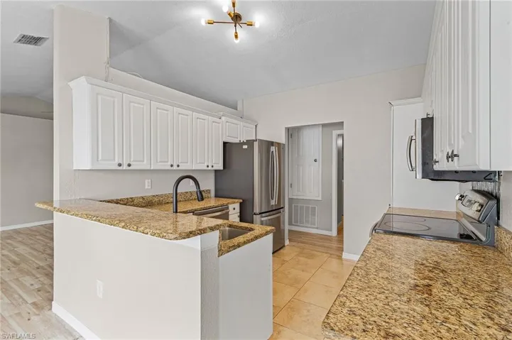Kitchen featuring white cabinetry, granite countertops, stainless steel appliances, kitchen peninsula, light tile flooring, and vaulted ceiling