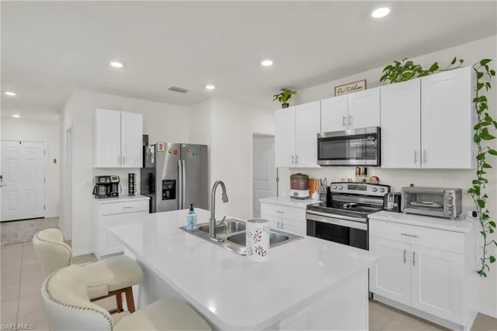 Kitchen with light tile patterned flooring, stainless steel appliances, a kitchen breakfast bar, white cabinetry, and recessed lighting