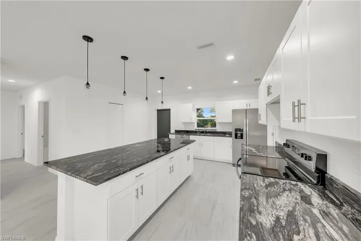 Kitchen featuring dark stone countertops, decorative light fixtures, appliances with stainless steel finishes, white cabinets, and a center island