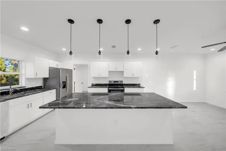 Kitchen featuring dark stone countertops, decorative light fixtures, stainless steel appliances, a kitchen island, and recessed lighting