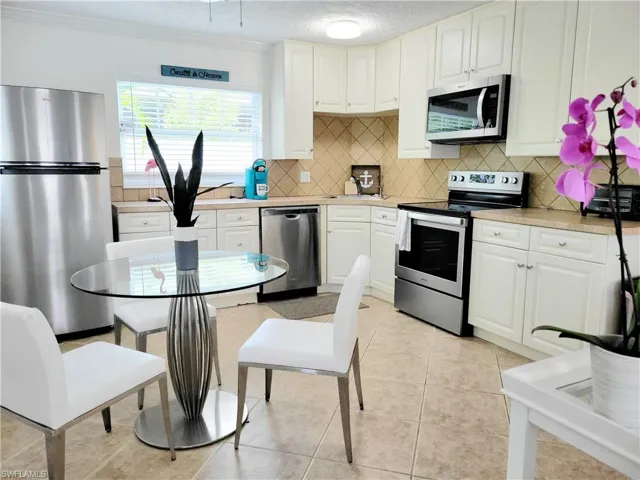 Kitchen featuring stainless steel appliances, light countertops, light tile patterned floors, white cabinetry, and ornamental molding