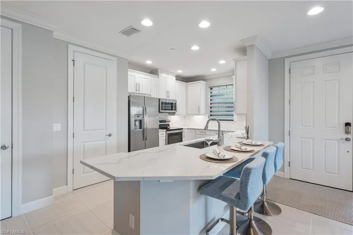Kitchen featuring kitchen peninsula, stainless steel appliances, light stone countertops, white cabinets, and light tile floors